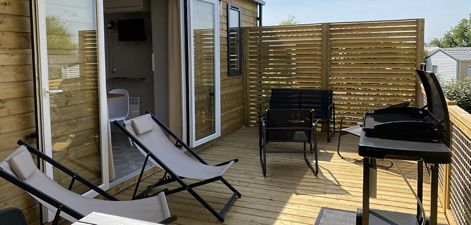 The half covered terrace with gas plancha, garden furniture and deckchairs of the mobile home Premium Garden side
