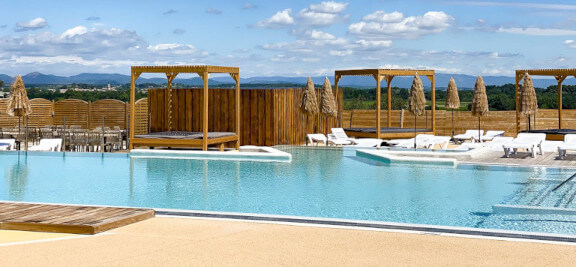 Waterlandschap met zwembad en ligstoelen op camping Les Amandiers bij Pézenas in Castelnau de Guers