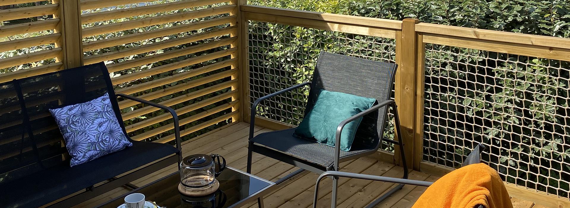 Het halfoverdekte terras met tuinmeubelen en ligstoelen in de aan de tuin grenzende mobil-home Premium, te huur op camping Les Amandiers in Hérault