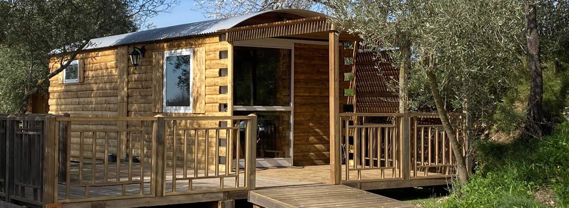 Vue extérieure de la roulotte Arizona et sa terrasse couverte, en location hébergement insolite au camping les Amandiers dans l’Hérault